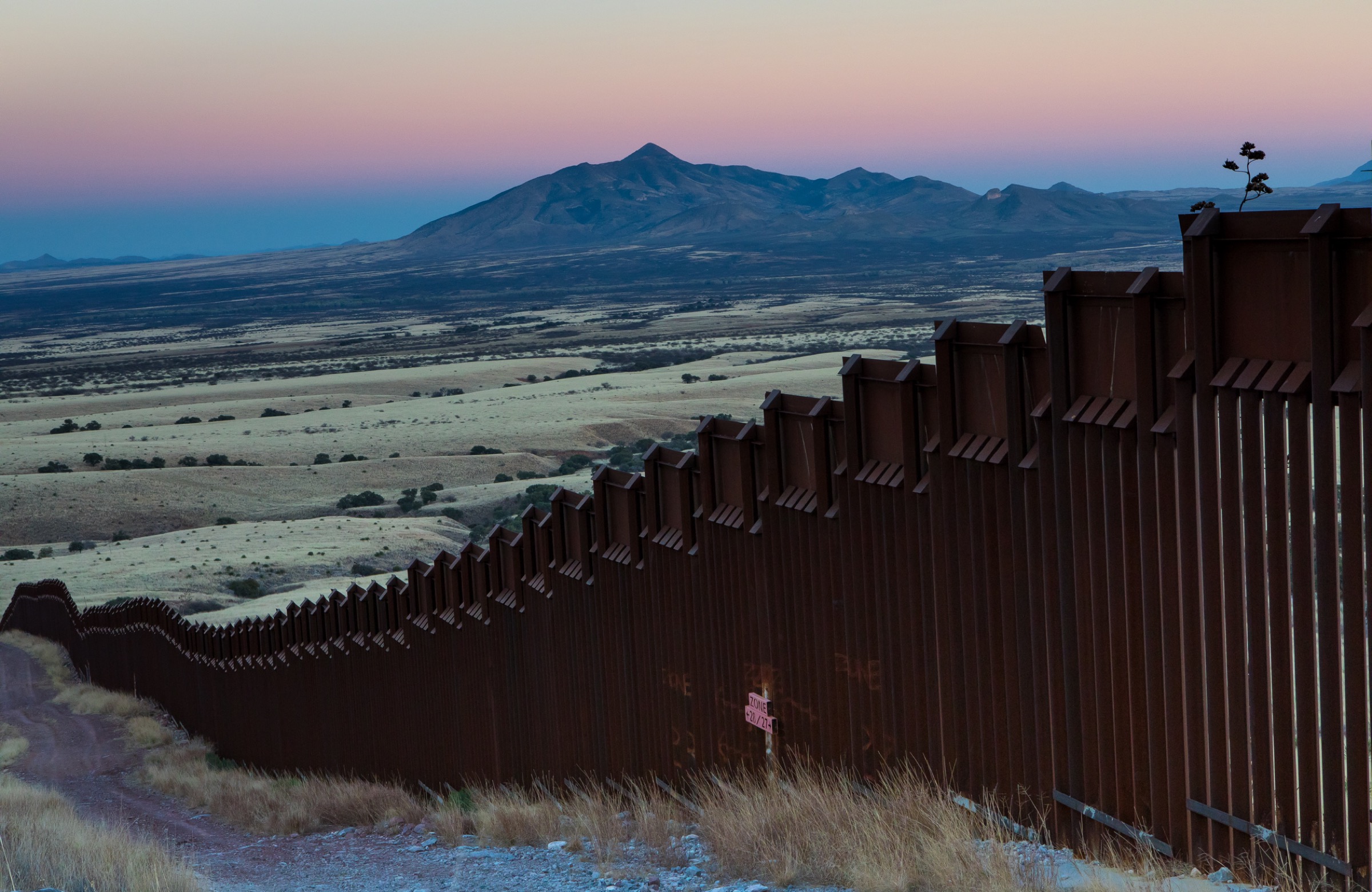 This section of border wall, originally constructed in 2008, stretches from the west bank of the San Pedro River into the foothills of the Huachuca Mountains in Arizona, a critical wildlife corridor between Sky Islands like the one visible in the background, in Sonora, Mexico. Photograph by Krista Schyler