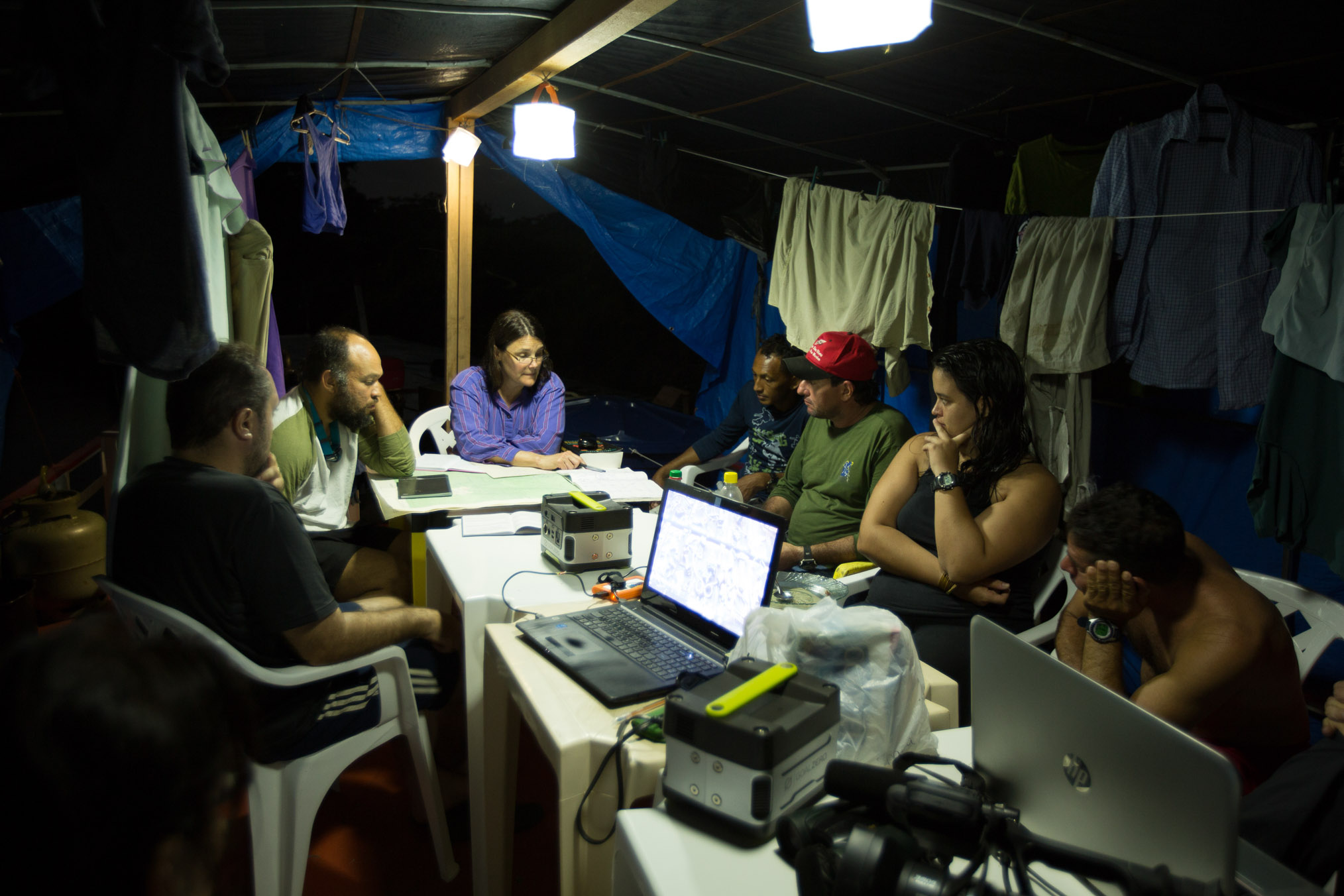 Surrounded by their drying laundry, the expedition team gathers for an evening meeting illuminated by solar lanterns on the second level of the houseboat.