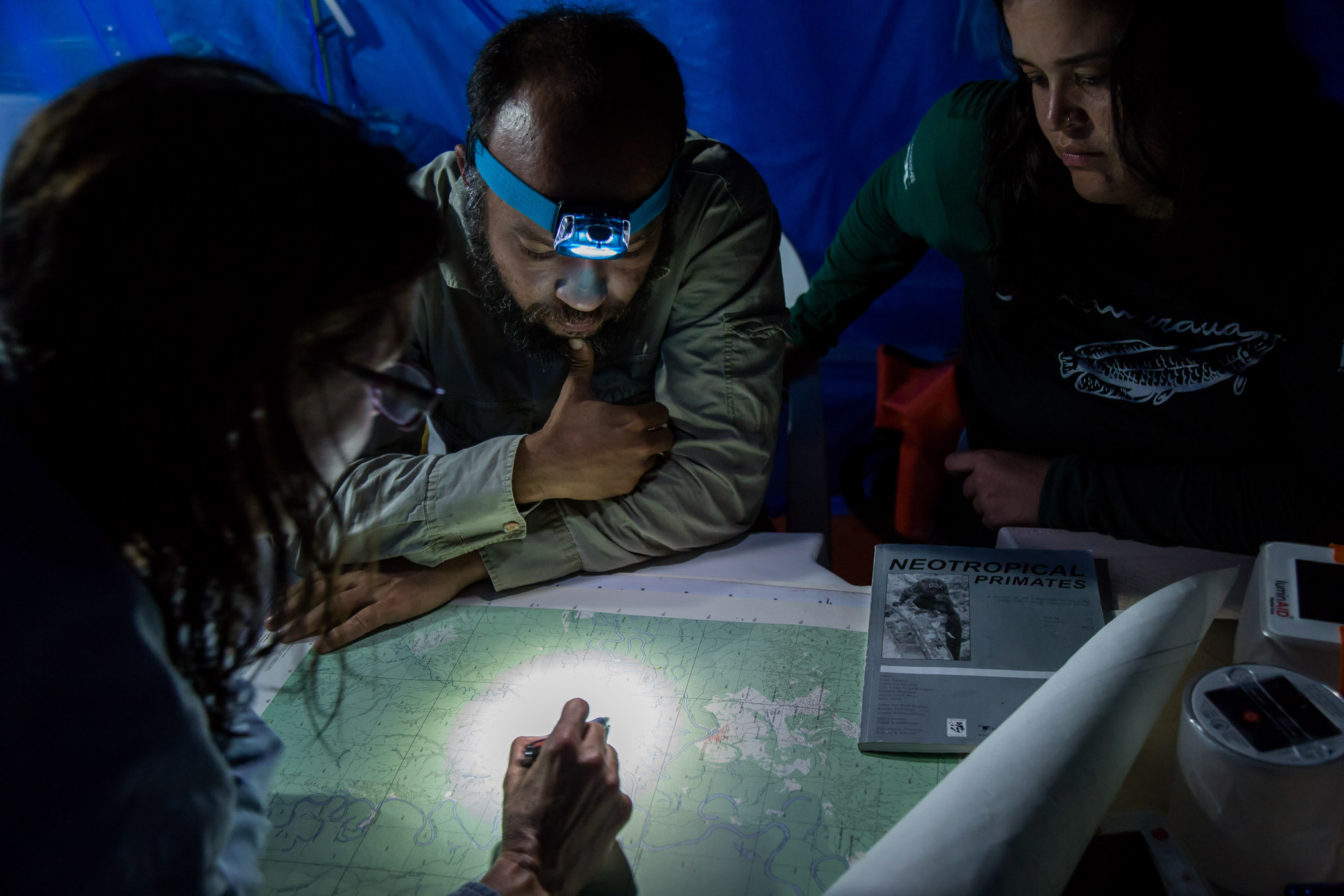 Scientists Laura Marsh (far left), Felipe Ennes, and Lísley Lemos study maps to determine the best areas to survey along the Eiru River.