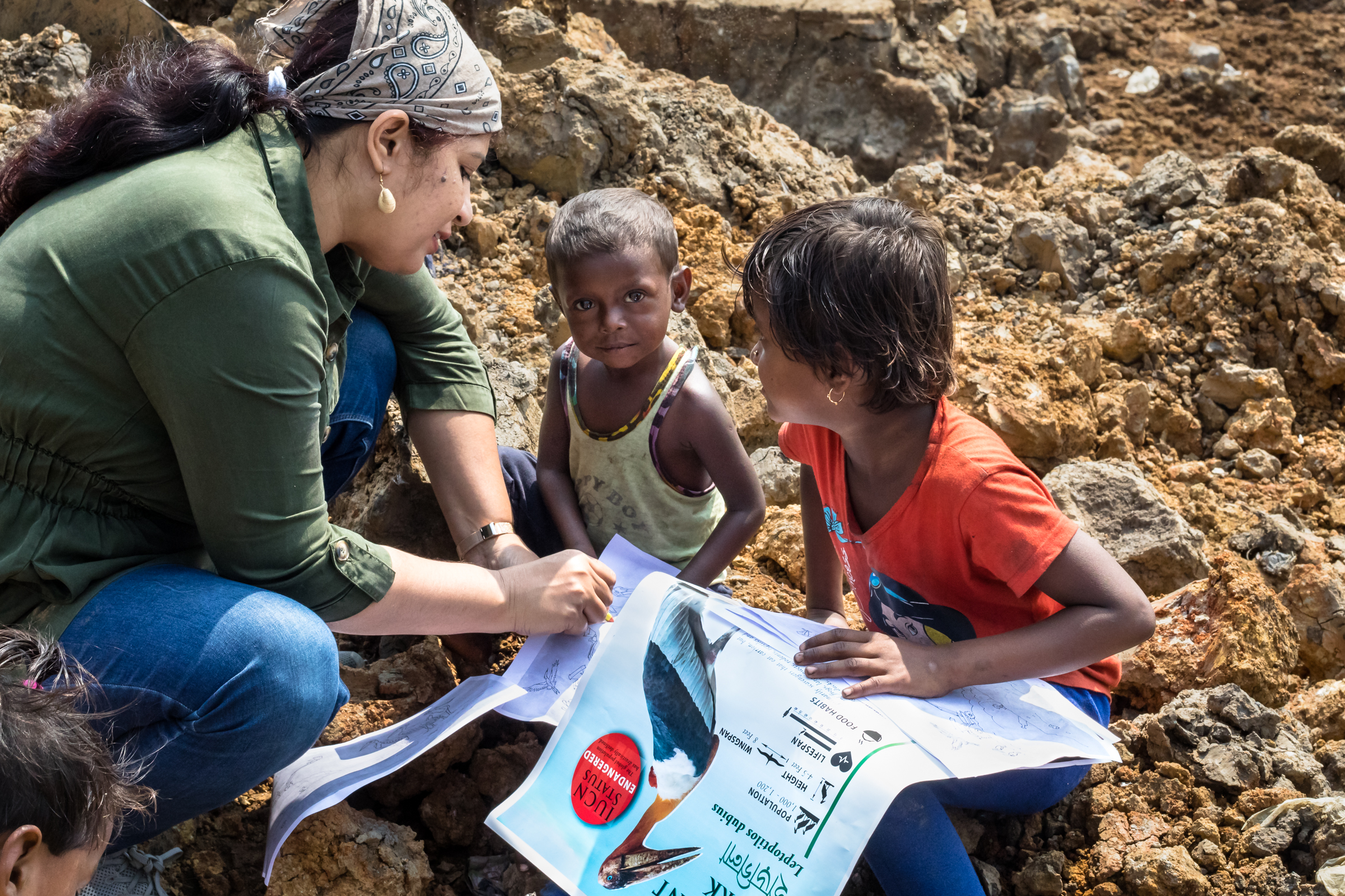 Purnima Devi Barman presents informational posters, coloring pages, and food to the people living and working in the sprawling landfill with the goal of raising awareness for the greater adjutants.