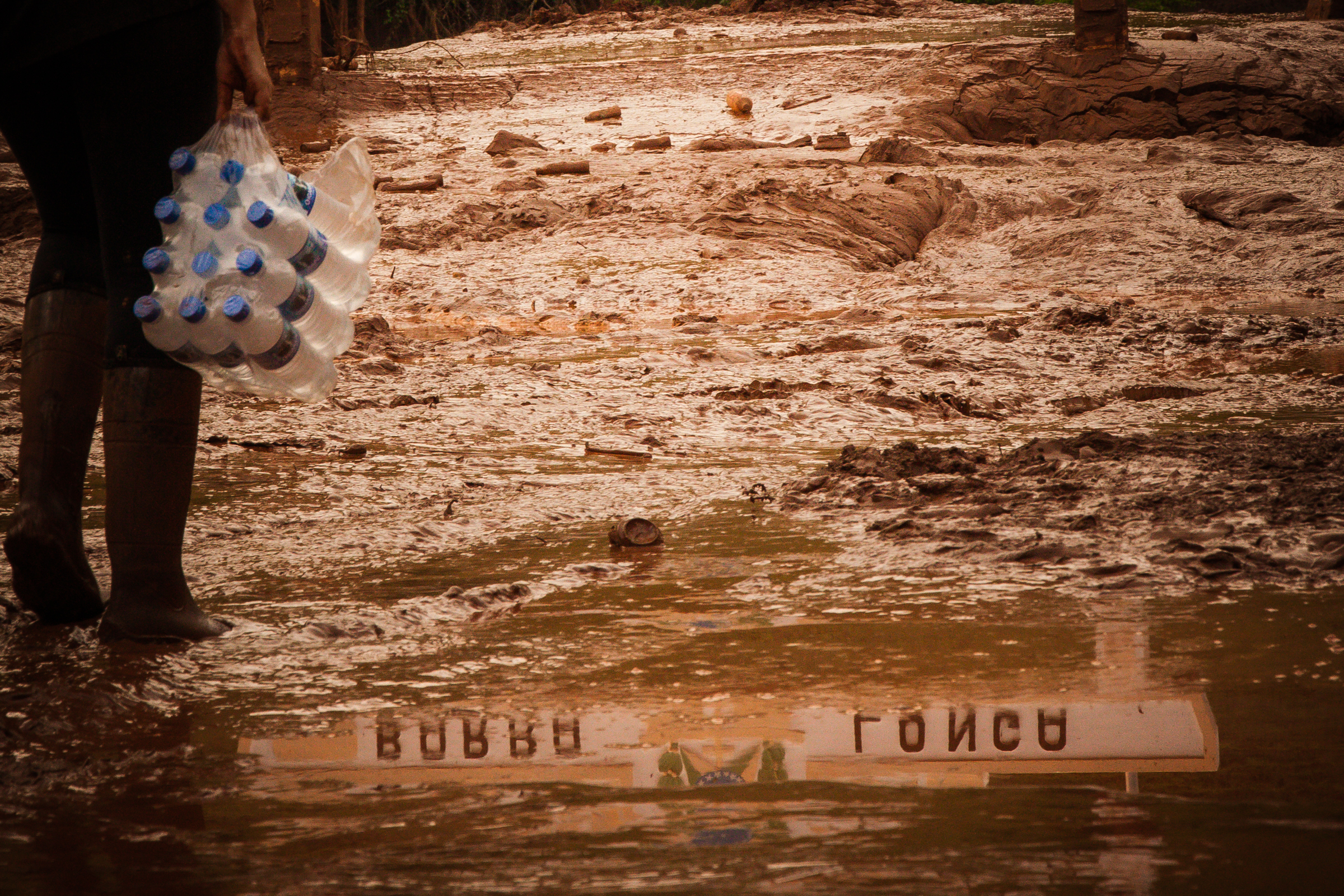 A resident of Barra Longa City carries water down a muddy street days after a tailings dam ruptured, killing 19 people and destroying the Doce River.