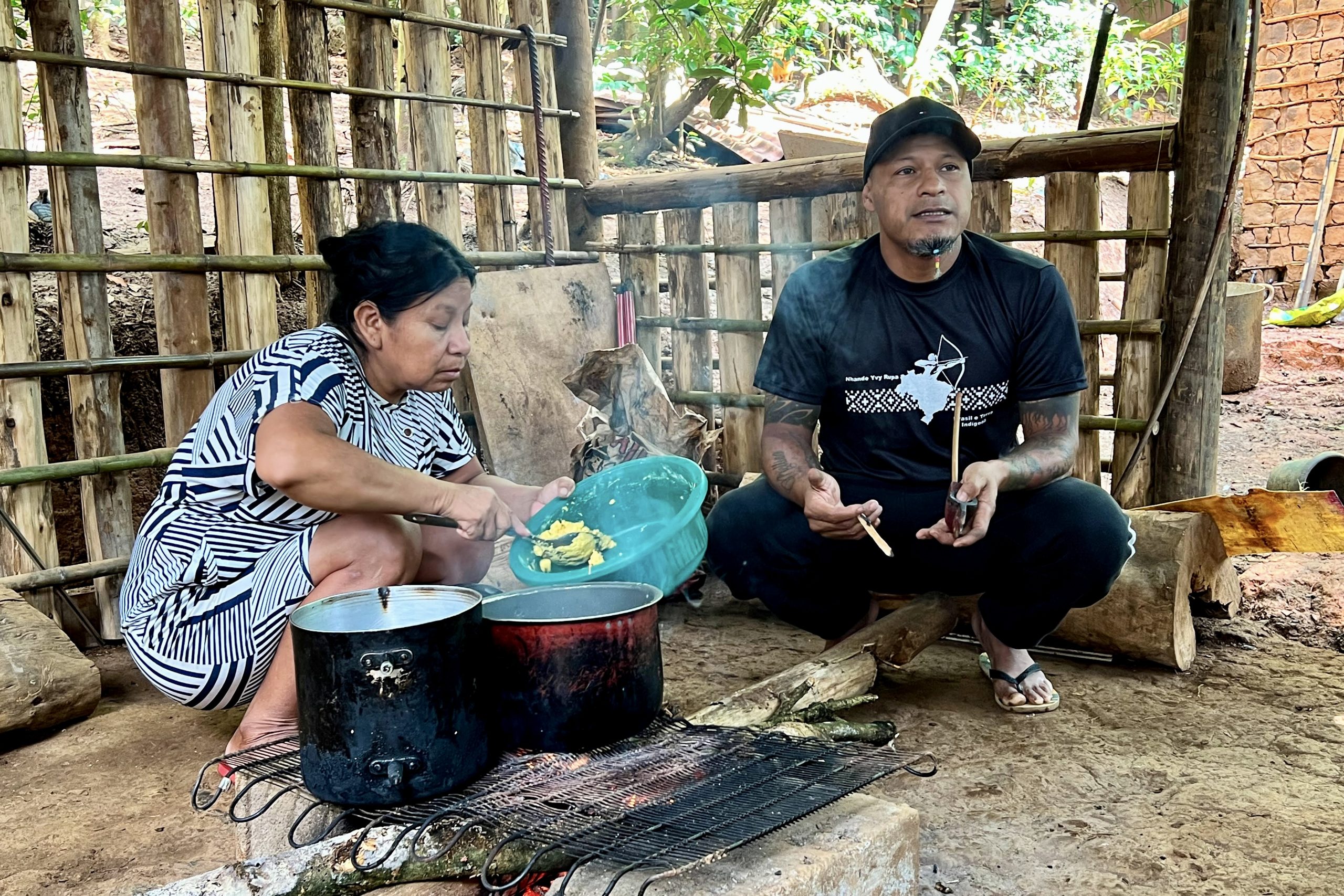 Guarani leader Jurandir Karai Jekupe (right) holds a traditional pipe close to the communal fire where a woman prepares a corn-based meal. Photograph by Sofia Moutinho