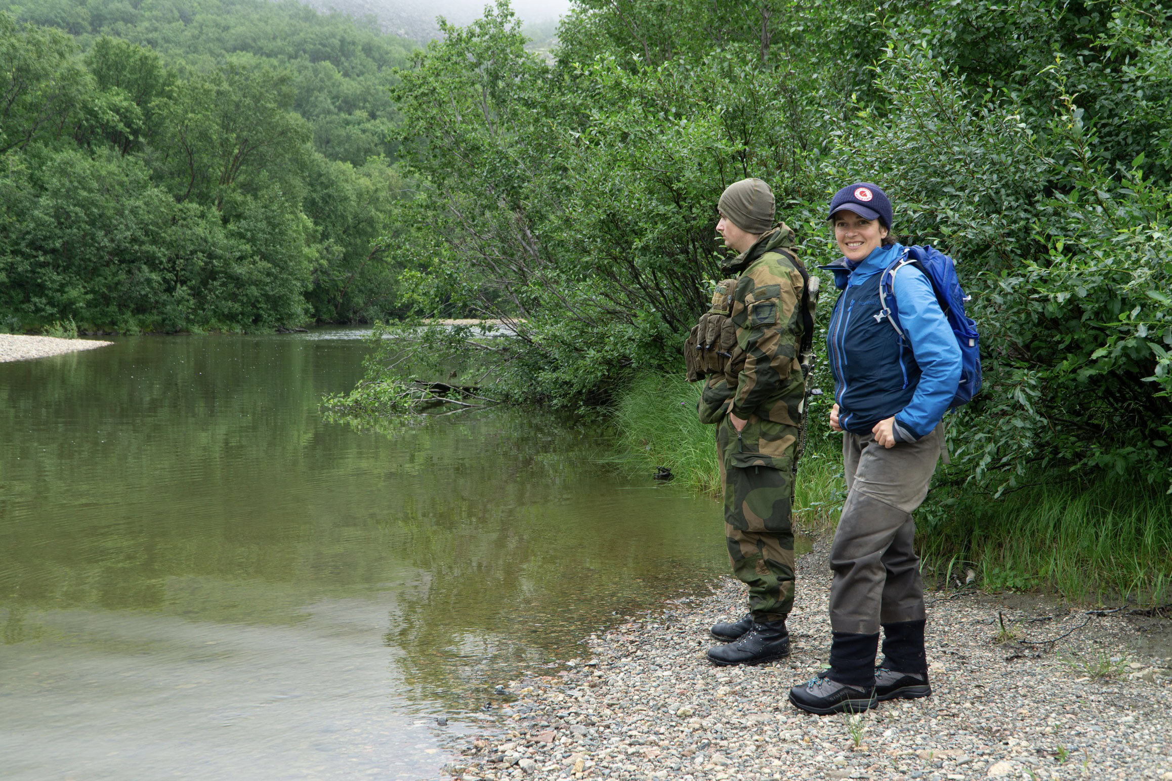 The border between Norway and Russia partly runs through the Grense Jakobselv, a boundary that shifts as the deepest part of the river shifts. No one is allowed to cross the border without permission. Marine ecologist Kathy Dunlop visits the river for fieldwork accompanied by a Norwegian soldier. Photo by Jude Isabella